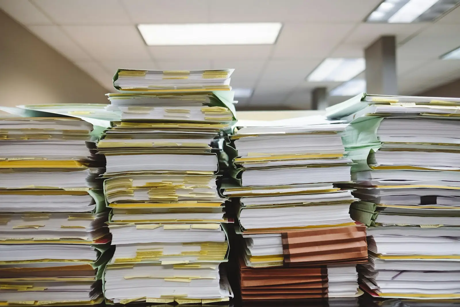 Tall stacks of paper files with yellow tabs on an office desk