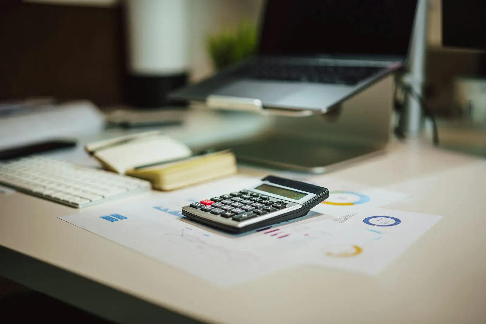 A calculator on printed financial reports beside a laptop